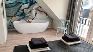 Un baño moderno con una bañera independiente, una silla y toallas sobre un banco.