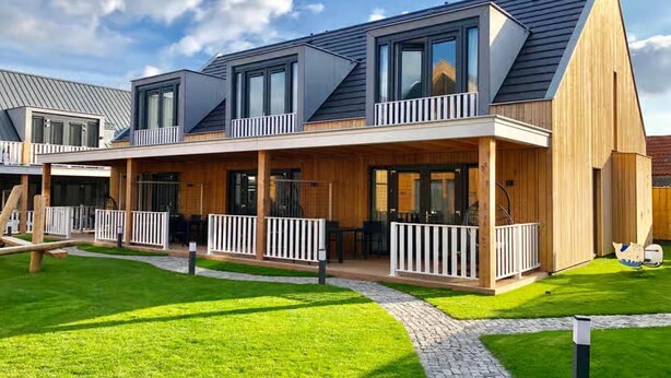 Une maison moderne à deux étages, dotée d’un patio couvert, d’une pelouse bien entretenue et offrant une vue sur un ciel dégagé.