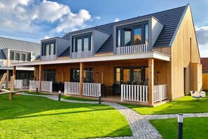 Een modern huis met twee verdiepingen, een overdekt terras, een verzorgd gazon en een heldere lucht.