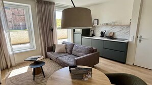 Een moderne woonkamer met een bank, salontafel en eettafel. Er is een keukenhoek met een spoelbak en kastjes.