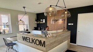 Een receptiebalie met 'WELKOM' aanduiding, een moderne hanglamp, een houten wandpaneel en een deur.