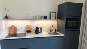 A modern kitchen with a marble countertop, dark cabinetry, a built-in oven, and a coffee maker. - Lodge with beautiful view of garden (Zoutelande)