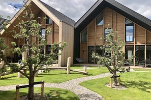 A modern building with wooden exterior, large windows, and a paved courtyard with trees and seating areas. - Beautiful lodge in the center of Zoutelande. (Zoutelande)