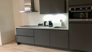 A modern kitchen with a stainless steel range hood, a built-in oven, and a coffee maker on the countertop. - Lodge with beautiful view of the church and dunes. (Zoutelande)