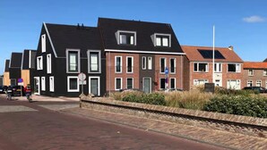 A row of modern houses with a mix of brick and dark-colored facades, a clear sky, and a paved street with a cyclist. - Lodge with beautiful view of the church and dunes. (Zoutelande)