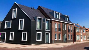 A modern two-story house with a black facade and white window frames, featuring a sloped roof and a brick extension. - Beautiful lodge suitable for 2 people. (Zoutelande)
