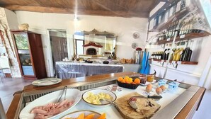 Un buffet de petit-déjeuner proposant une variété d’aliments, notamment des viandes, des fruits et des œufs, dans une pièce bien éclairée, dotée de poutres en bois et d’un grand miroir.