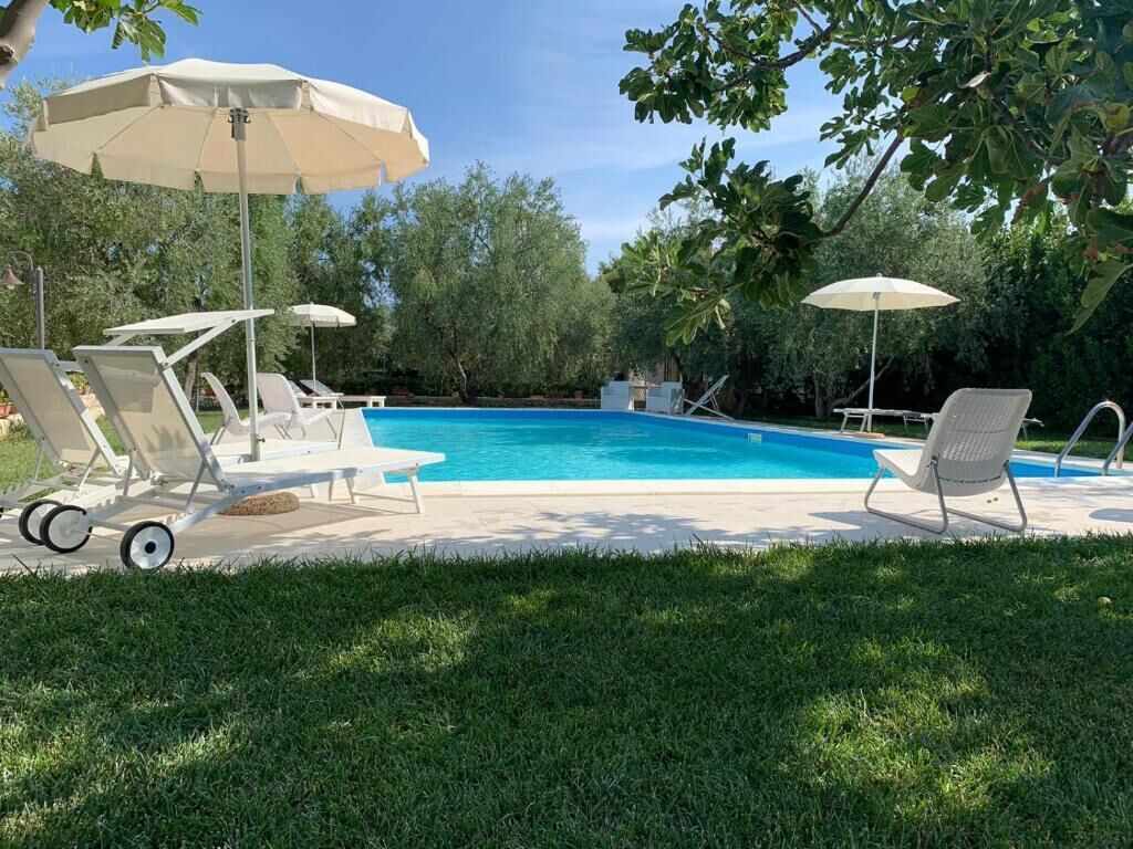 Une piscine entourée d’arbres, avec des chaises longues et des parasols.