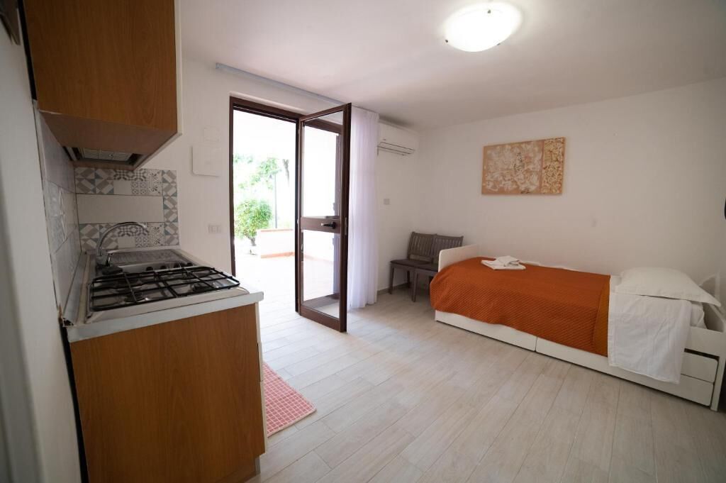 Habitación compacta con kitchenette, cama y puerta corrediza que da a un espacio exterior.