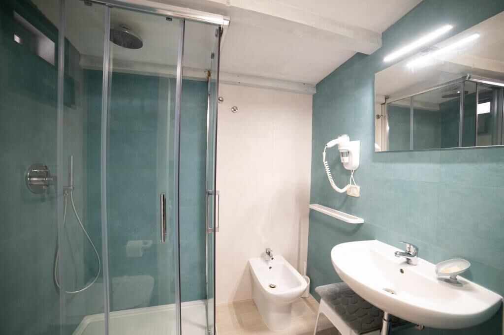 A bathroom with a glass-enclosed shower, a white pedestal bidet, and a white sink with a mirror above it.