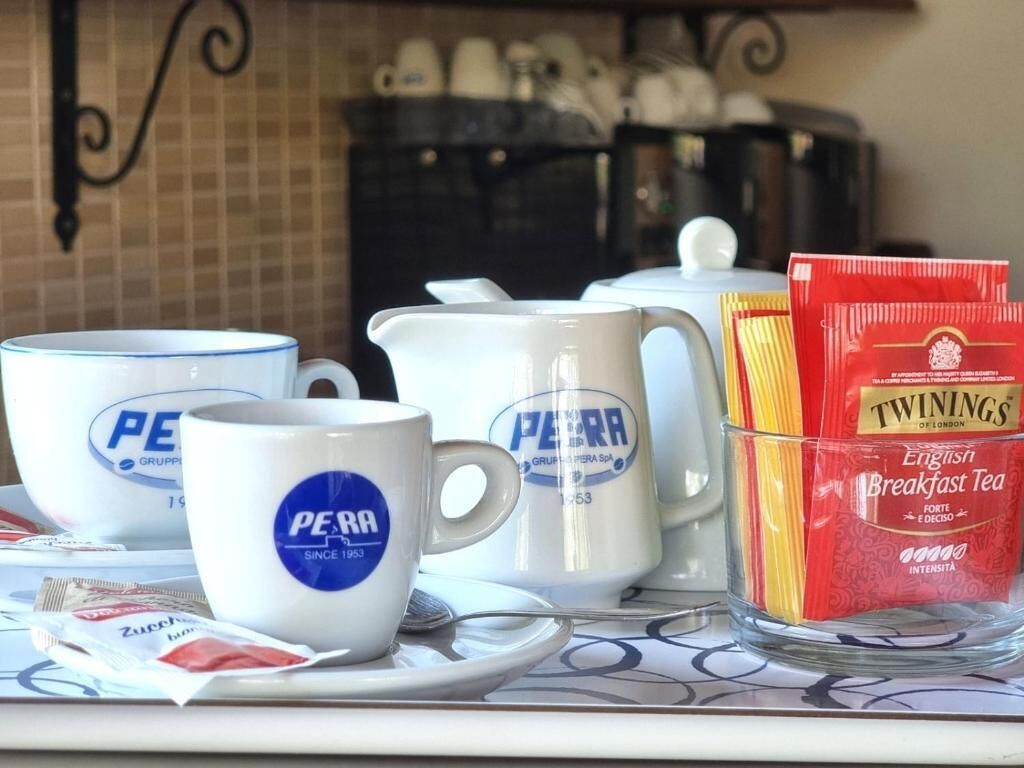 A breakfast setup with two white mugs labeled "PERA", a white teapot, a glass of yellow straws, and a red packet of Twinings English Breakfast Tea.