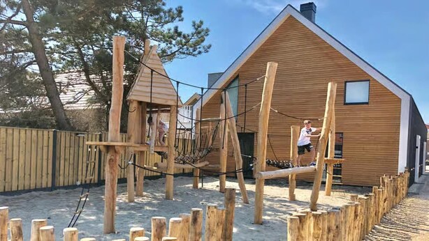 En lekställning i trä med en repbro och ett litet trähus i bakgrunden.
