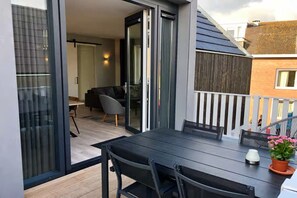 A balcony with a table and chairs, a potted plant, and a sliding glass door leading to an interior space with a sofa and a table. - Lodge with view of the church and dunes (Zoutelande)