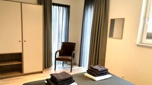 Habitación de hotel con cama, una silla, armario y ventana con cortinas.