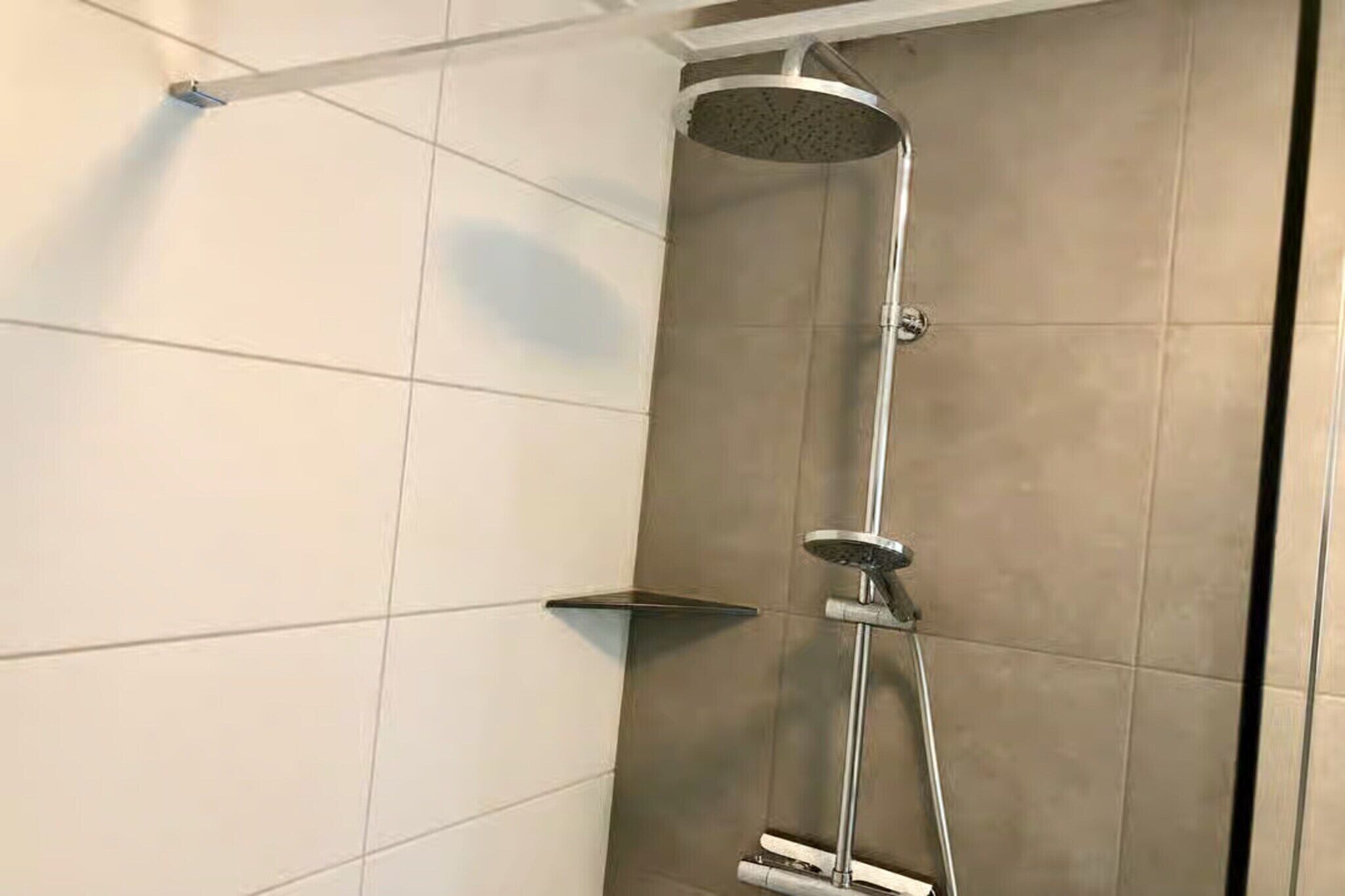 A modern shower with a handheld showerhead and a wall-mounted rain showerhead.