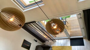 Una sala de estar moderna con dos lámparas colgantes grandes de estilo farol, un sofá de cuero oscuro, una mesita y vistas a una terraza exterior a través de un gran ventanal corredero.