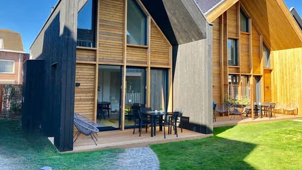 Una casa moderna con techo inclinado, ventanas amplias y un patio con mobiliario exterior.