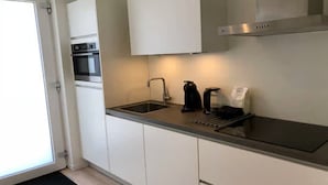 A modern kitchen with white cabinets, a stainless steel range hood, a sink, and a coffee maker. - 4-person luxury lodge in Zoutelande (Zoutelande)