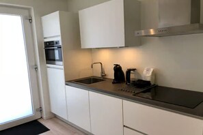 Eine moderne Küche mit weißen Schränken, einer Edelstahl-Dunstabzugshaube, einem Spülbecken und einer Kaffeemaschine.