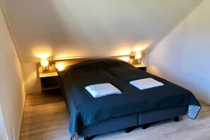 A bedroom with a dark-colored bed, two bedside lamps, and a small bedside table. - 4-person luxury lodge in Zoutelande (Zoutelande)