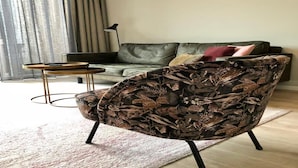 A living room with a sofa, a patterned armchair, a small round table, and a floor lamp. - 4-person luxury lodge in Zoutelande (Zoutelande)