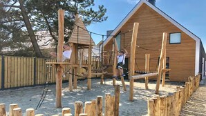 Una construcció de fusta per jugar, amb ponts de corda i una casa de fusta al fons.