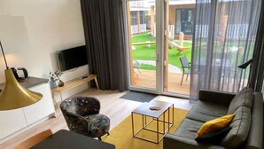 Un saló modern amb un sofà, una butaca, televisió i una porta corredissa de vidre que dona a un patiec.