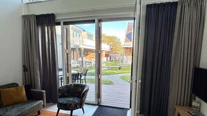 Een moderne woonkamer met een bank, fauteuil en salontafel. Er is een schuifdeur die leidt naar een terras met een tafel en stoelen.
