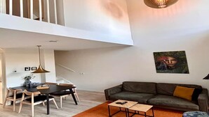 Een moderne woonkamer met een eethoek, een bank en een hanglamp.
