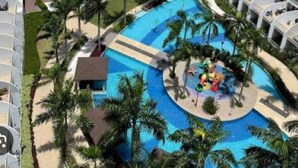 Een hoog hotel met meerdere balkons en een zwembad in het midden, omgeven door palmbomen.