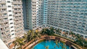 Un hotel moderno con numerosi balconi e una piscina centrale circondata da palme.