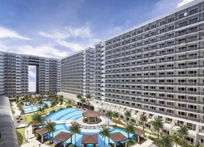 A high-rise hotel with multiple balconies, a swimming pool, and a landscaped area with palm trees.