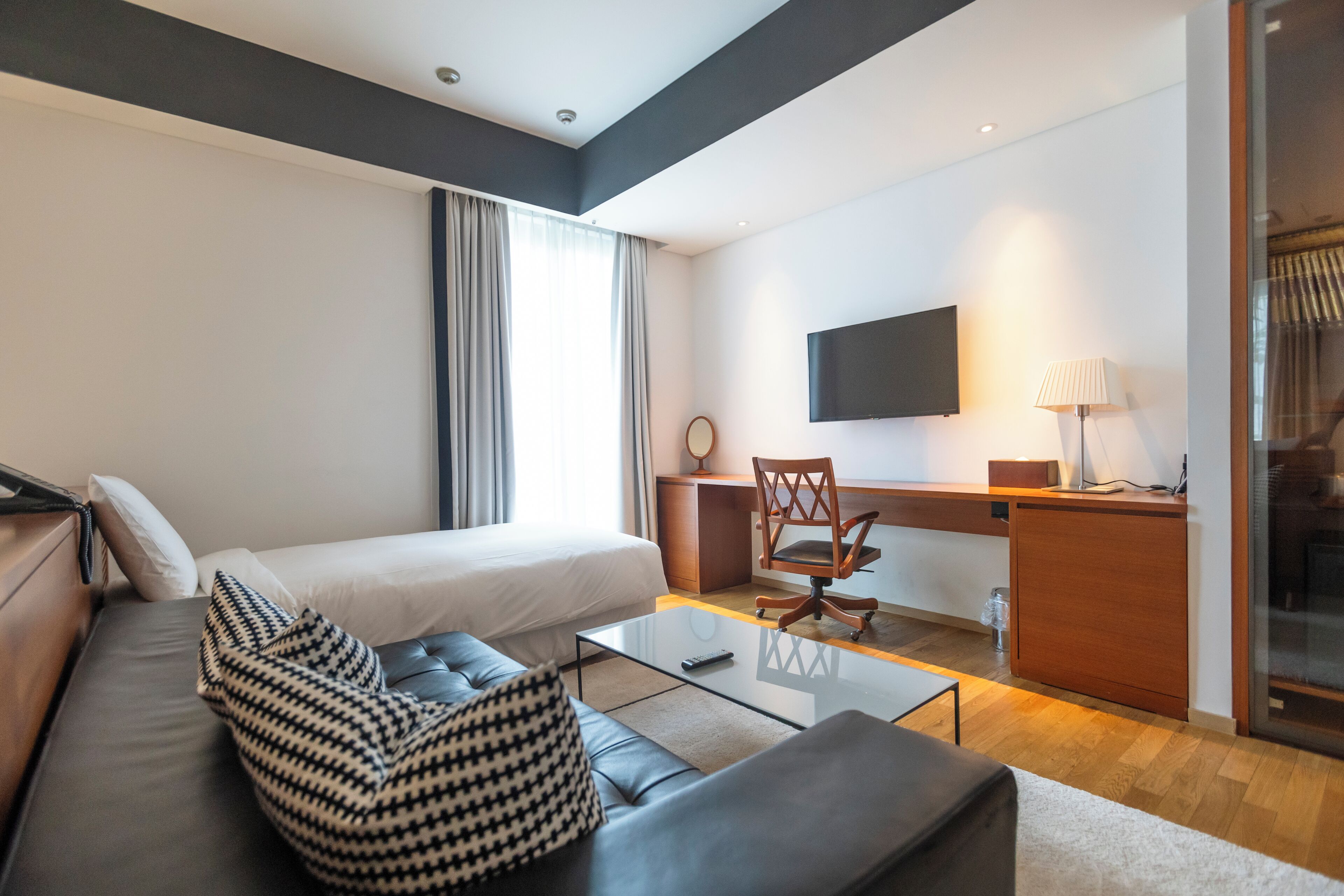 A modern hotel room with a bed, a sofa, a desk, and a TV.