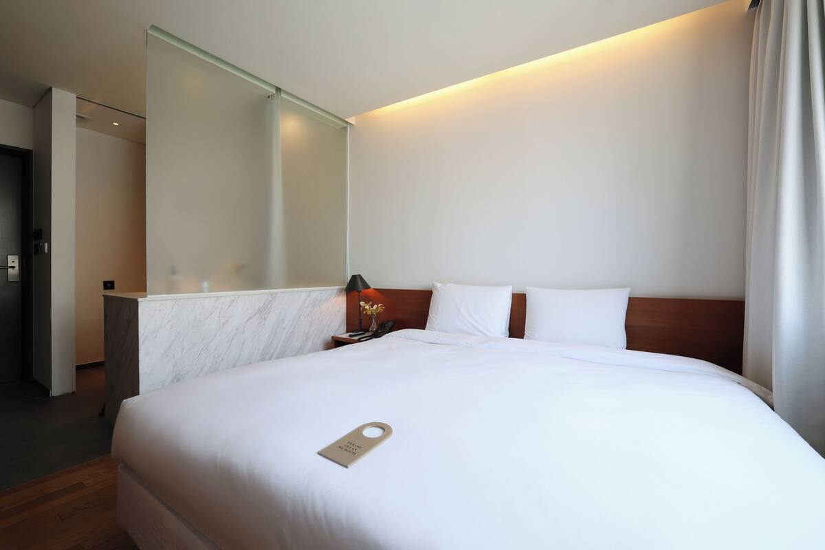 A hotel room with a large bed, a marble bedside table, a nightstand with a lamp, and a mirror on the wall.