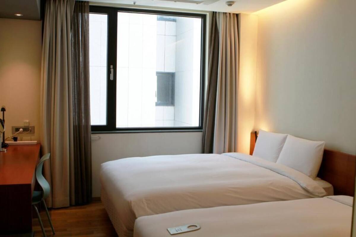 A hotel room with two beds, a desk, and a window with curtains.