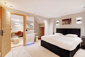 Ein modernes Schlafzimmer mit einem großen Bett, einer Holztür, einem Badezimmer und einer kleinen Sitzecke.