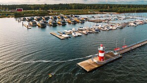 A marina with numerous boats docked, a pier with a lighthouse, and a forested landscape in the background. - Holiday home for six guests, Klitten (Klitten)