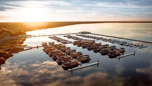 An aerial view of a marina with numerous docked boats and floating structures, surrounded by calm water and a forested shoreline. - Holiday home for six guests, Klitten (Klitten)