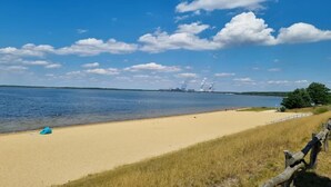 Une plage avec une clôture en bois, un rivage sablonneux et un ciel bleu clair parsemé de nuages.