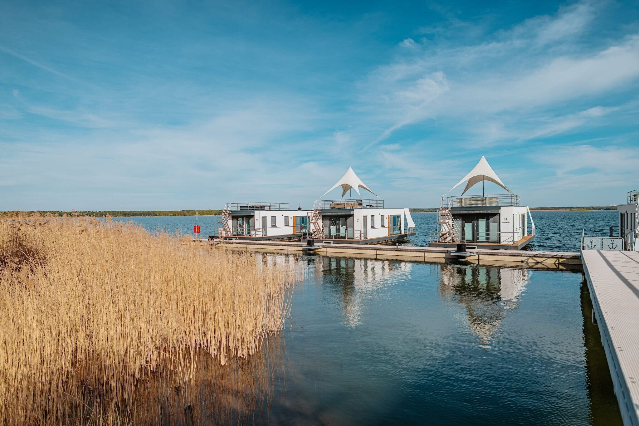 Een pand aan het water met drie moderne, witte, tentachtige constructies die aan een steiger liggen.