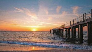 A pier extending into the ocean at sunset with waves gently lapping at the base. - Bright Base with Coastal Access (Ribnitz-Damgarten)