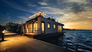 A modern houseboat with a deck, windows, and a railing, docked at a pier. - Bright Base with Coastal Access (Ribnitz-Damgarten)