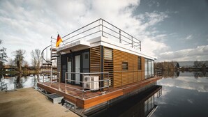 Uma casa flutuante com deck de madeira, janelas amplas e uma bandeira.