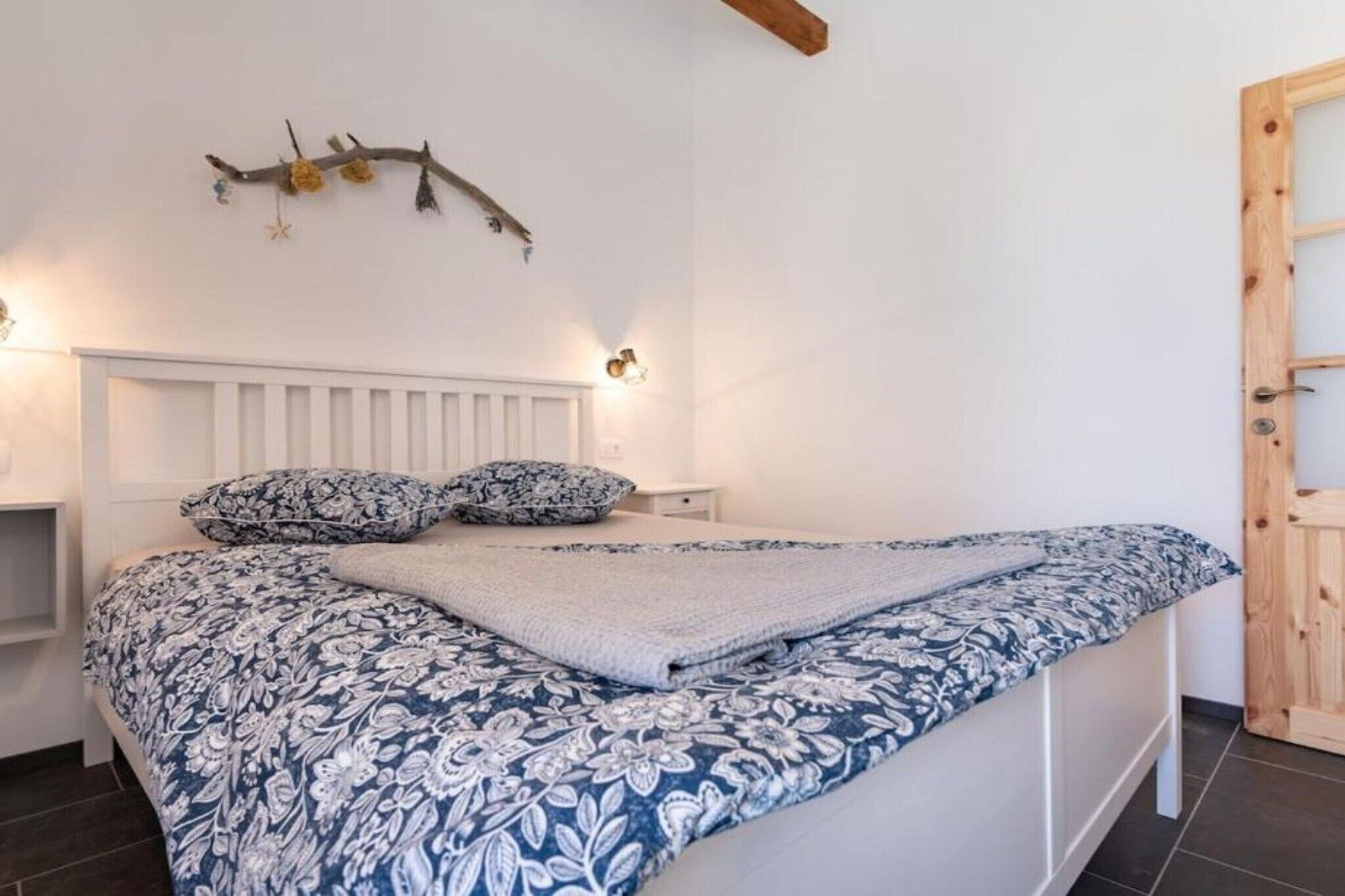 A bedroom with a white headboard, a bed with a blue and white floral bedspread, and a wooden door on the right.
