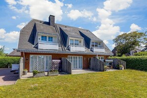 Een huis met twee verdiepingen, een schuin dak, een houten omheining en een gazon.