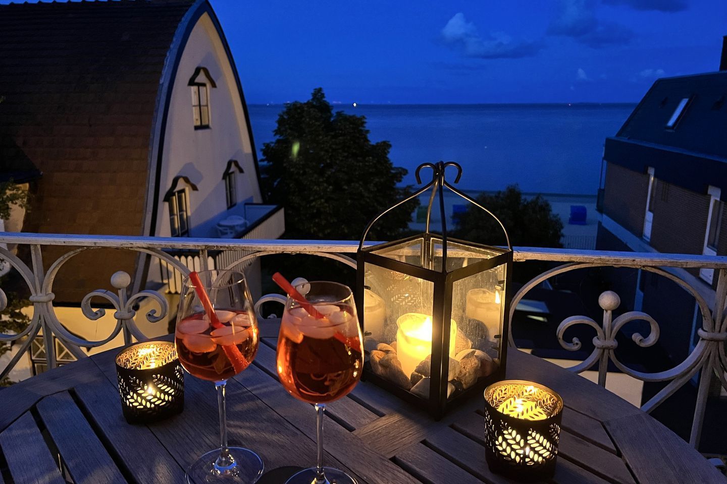 A balcony with two glasses of drink, a lantern, and a view of the sea.