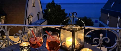 A balcony with two glasses of drink, a lantern, and a view of the sea.