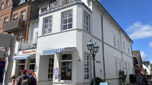 A white building with a blue-striped awning, a sign reading 'Adenauer & Co.', and a street lamp. - Sandwall 14, Whg. 6, Sandwallkoje - Holiday apartment with 3 rooms on the Sandwall (Wyk auf Föhr)