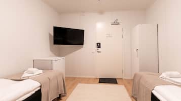 Habitación de hotel con dos camas, un televisor montado en la pared, un armario blanco y una puerta con picaporte.