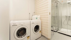 A laundry area with two Whirlpool washers, a glass shower enclosure, and a white tiled floor. - Lodge Finland Ylläs (Kolari)